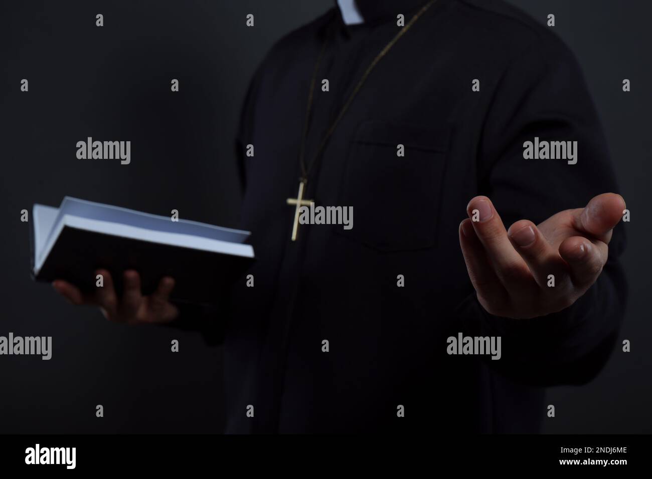 Priest in cassock with Bible on black background, closeup Stock Photo