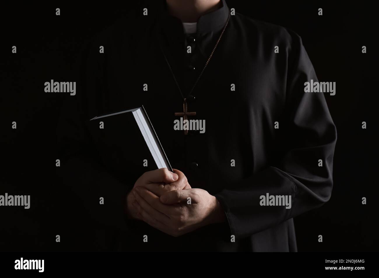 Priest with Bible on dark background, closeup Stock Photo