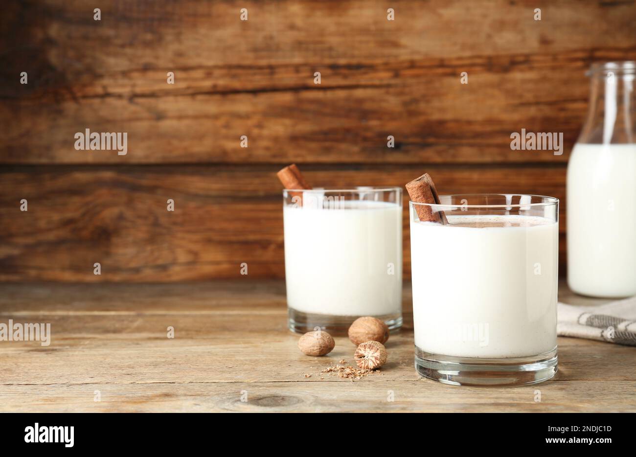 Milk with nutmegs and cinnamon on wooden table. Space for text Stock