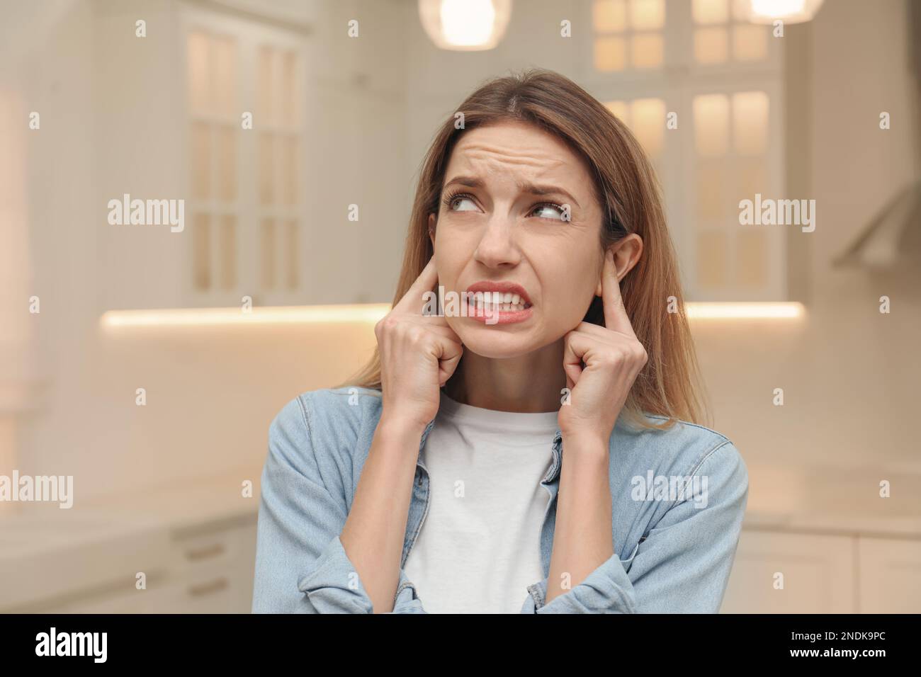 Emotional young woman covering her ears with fingers at home Stock
