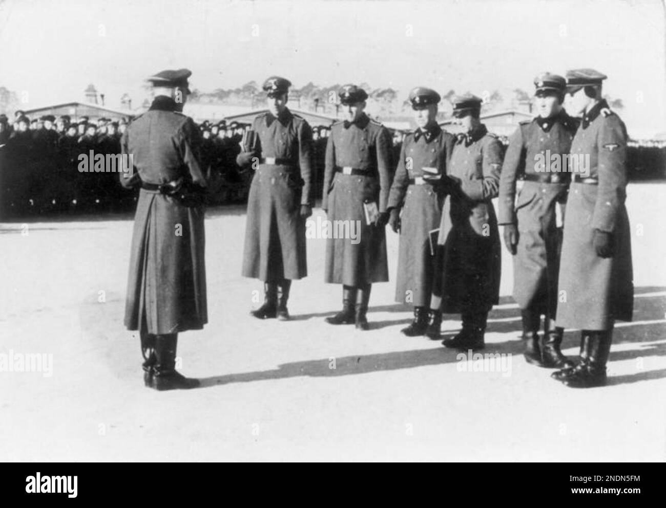Members of the Totenkopf camp guards unit at Sachsenhausen concentration camp. The prisoners can be seen lined up in the background. The Totenkopf guards unit were a separate unit within the SS and were responsible for the running of the concentration and extermination camps. They are distinguished by the death's head emblem on their lapel. The 3rd SS Panzer division carried the name Totenkopf but were a fighting unit not involved in the administration of the camps. By Bundesarchiv, Bild 183-78612-0010 / CC-BY-SA 3.0, CC BY-SA 3.0 de, https://commons.wikimedia.org/w/index.php?curid=5431255 Stock Photo