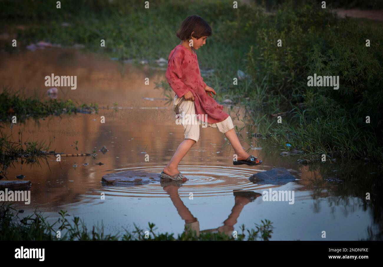 A Pakistani girl crosses a small river in a poor neighborhood on the  outskirts of Islamabad,