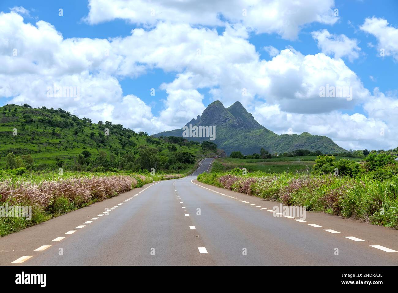 Asphalted road to the mountain against blue cloudy sky. Stock Photo