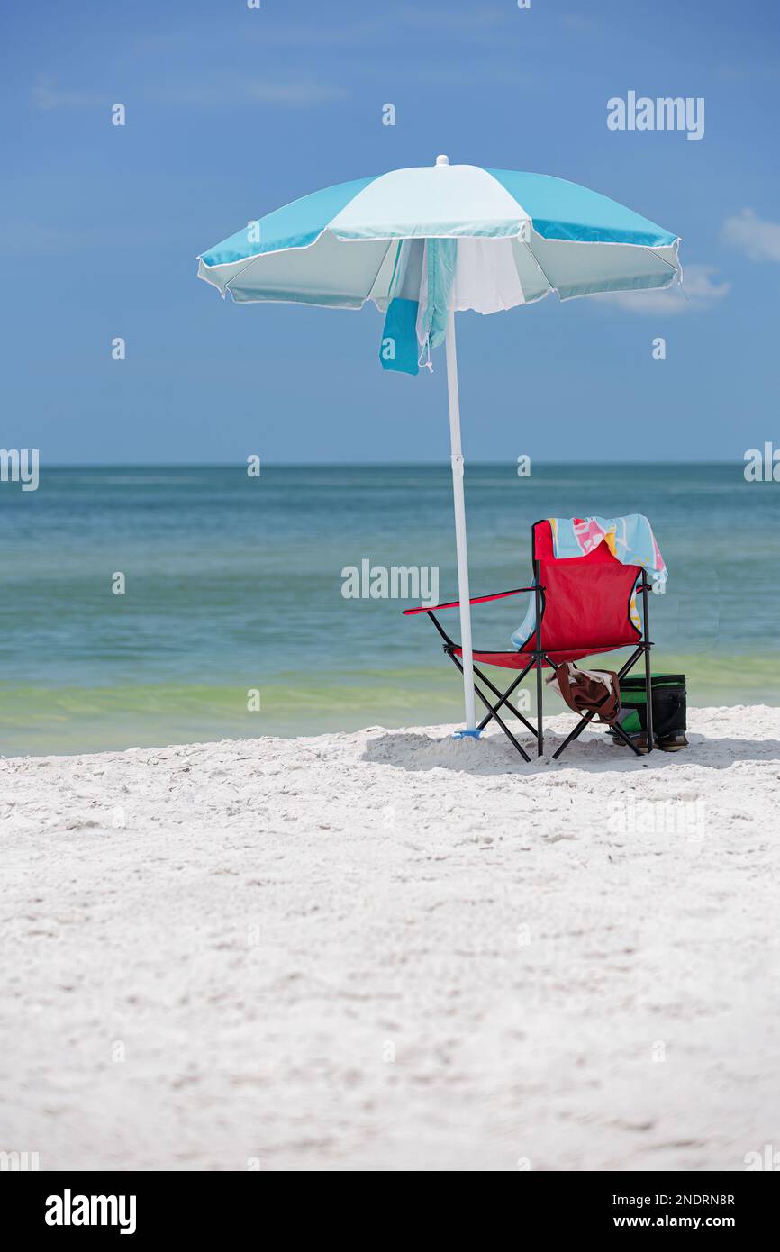 Beach chair umbrella in sand with cooler and towel at ocean with sky background Stock Photo