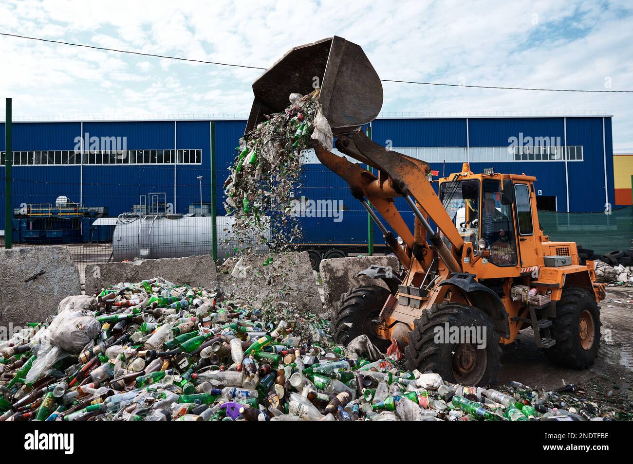 The bucket loader breaks glass bottles by dumping them out of the