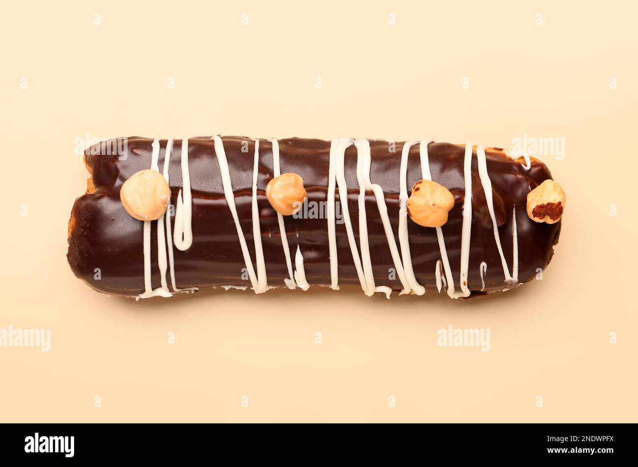 Delicious chocolate eclair with hazelnuts on beige background Stock Photo