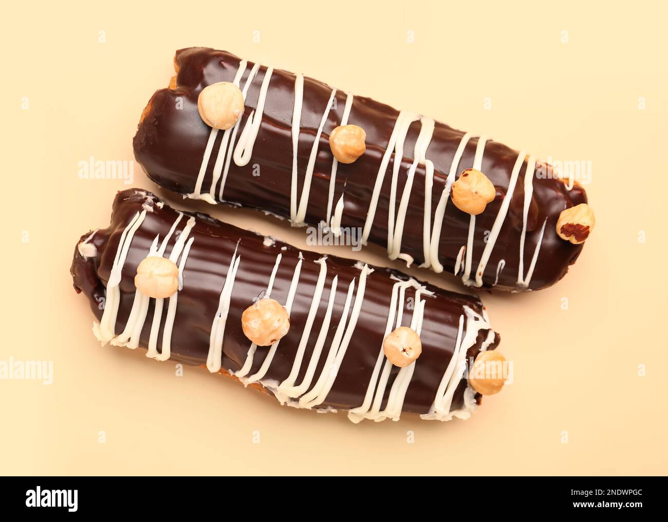 Delicious chocolate eclairs with hazelnuts on beige background Stock Photo