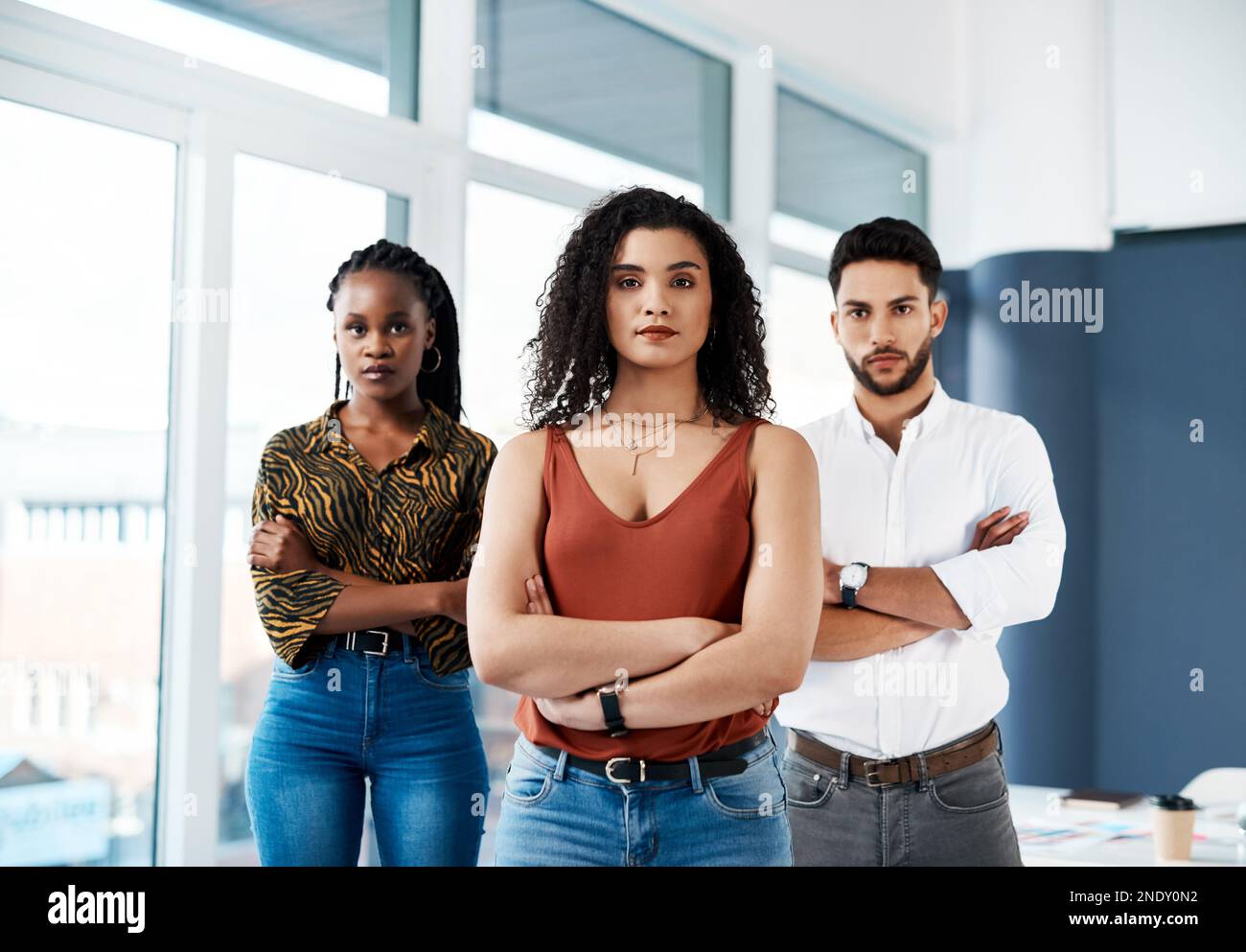 We will overcome any obstacle. Cropped portrait of an attractive young businesswoman standing with her arms crossed in front of her colleagues in the Stock Photo