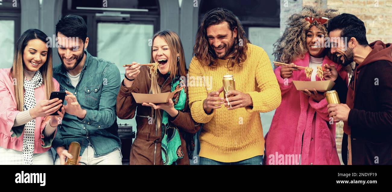 A group of millennials of various ethnicities eat takeout and drink beer under city porticos on a weekend afternoon. They are casually dressed and soc Stock Photo