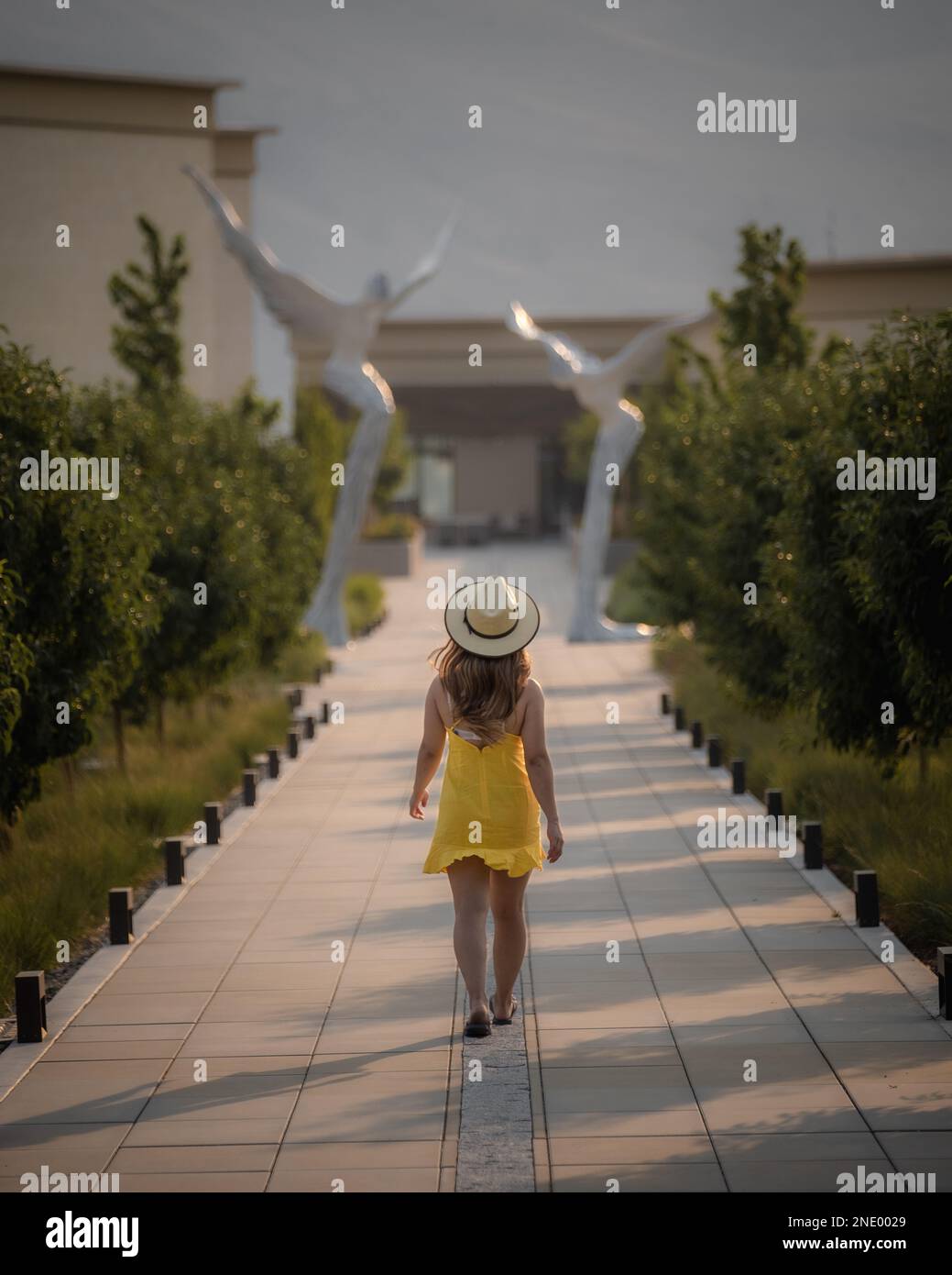 girl walking down a path wearing a yellow dress and hat Stock Photo