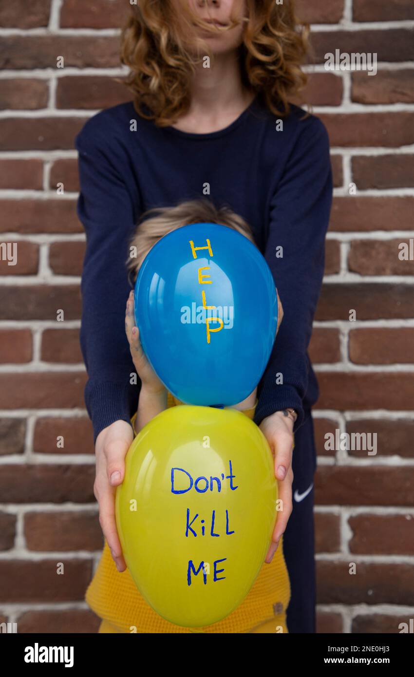 two unrecognizable people, adult and child, with blue yellow balloons with inscriptions do not kill me and help. Ukrainians are against war. Fear, dra Stock Photo