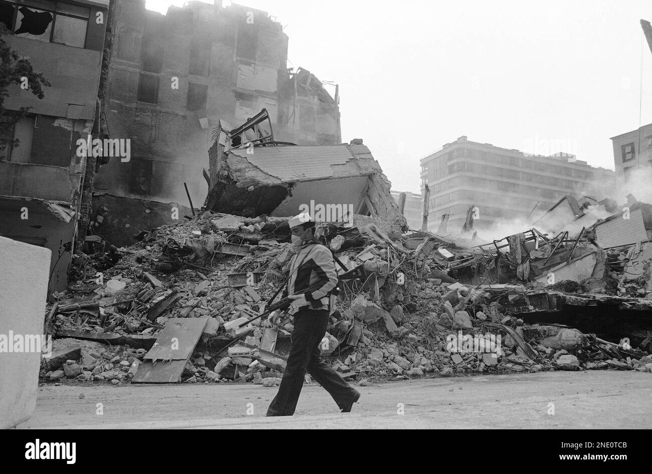 A man armed with a rifle walks down an earthquakeravaged street in