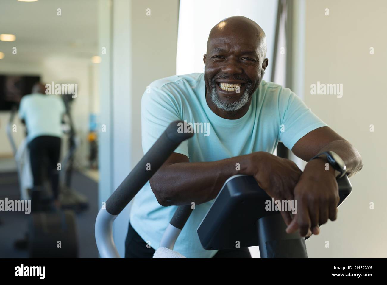 Portrait of african american senior man smiling while standing on elliptical machine at the gym. retirement senior lifestyle and living concept Stock Photo