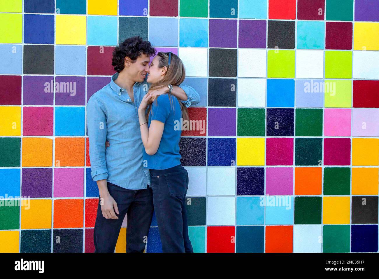 A young couple interlaced in front of colorful tiles Stock Photo
