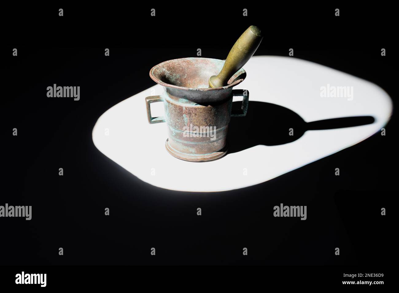 Bronze mortar and pestle covered with patina illuminated by a hard beam