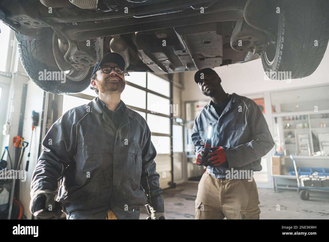 Medium shot of two mechanics inspecting car's underside. High quality photo Stock Photo