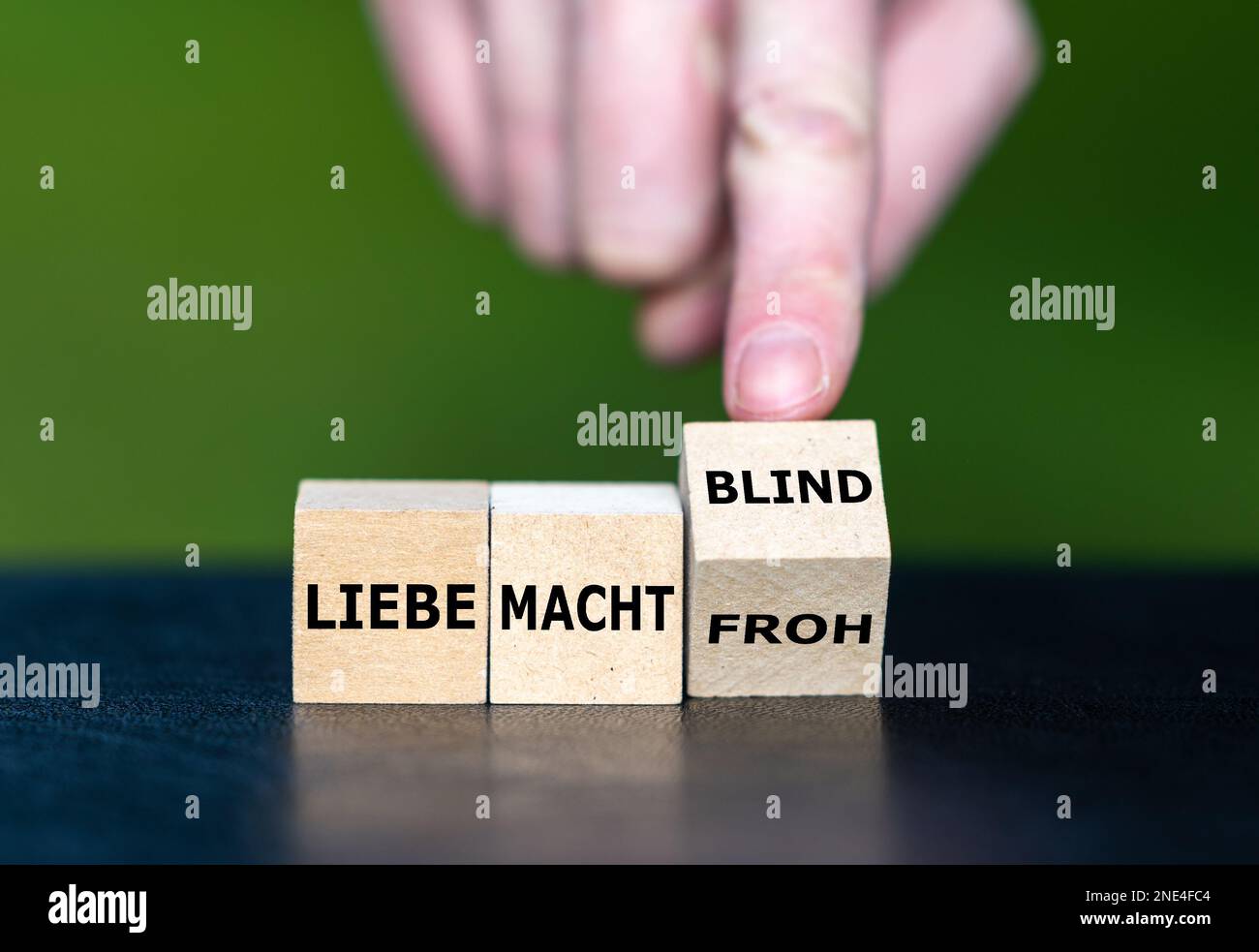Hand turns wooden cubes and changes the German saying 'liebe macht froh' (love makes happy) to 'liebe macht blind' (love makes blind). Stock Photo