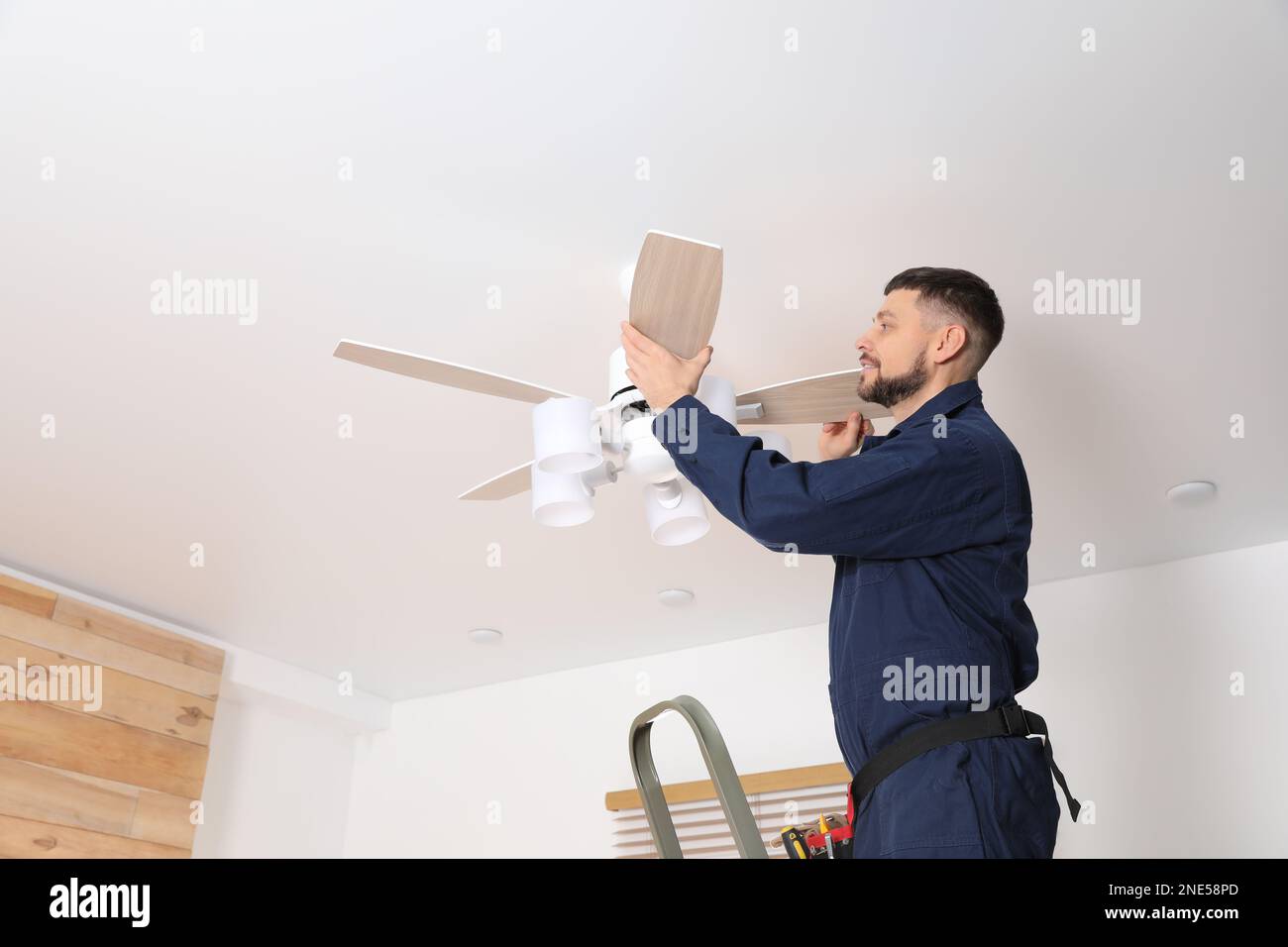 Electrician repairing ceiling fan indoors. Space for text Stock Photo