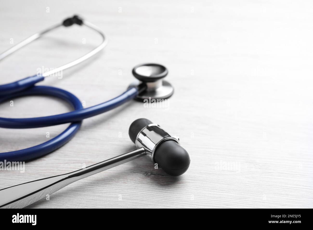 Reflex hammer with stethoscope on light wooden background, closeup