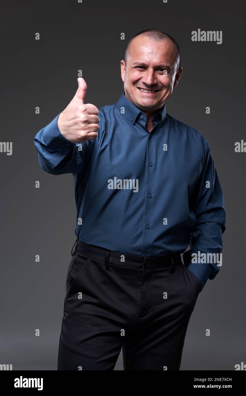 Happy businessman showing thumbs up sign, at the end of a done deal, isolated on gray background Stock Photo