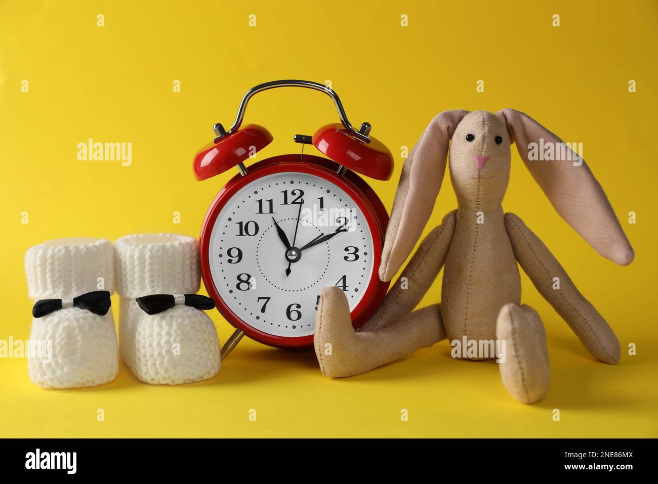 Alarm clock, bunny and baby booties on yellow background. Time to give