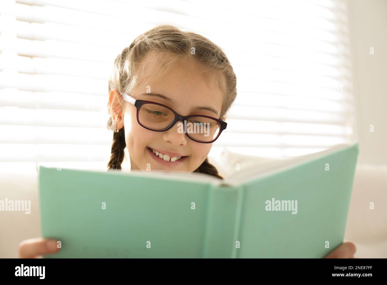 Cute little girl reading book near window at home Stock Photo - Alamy