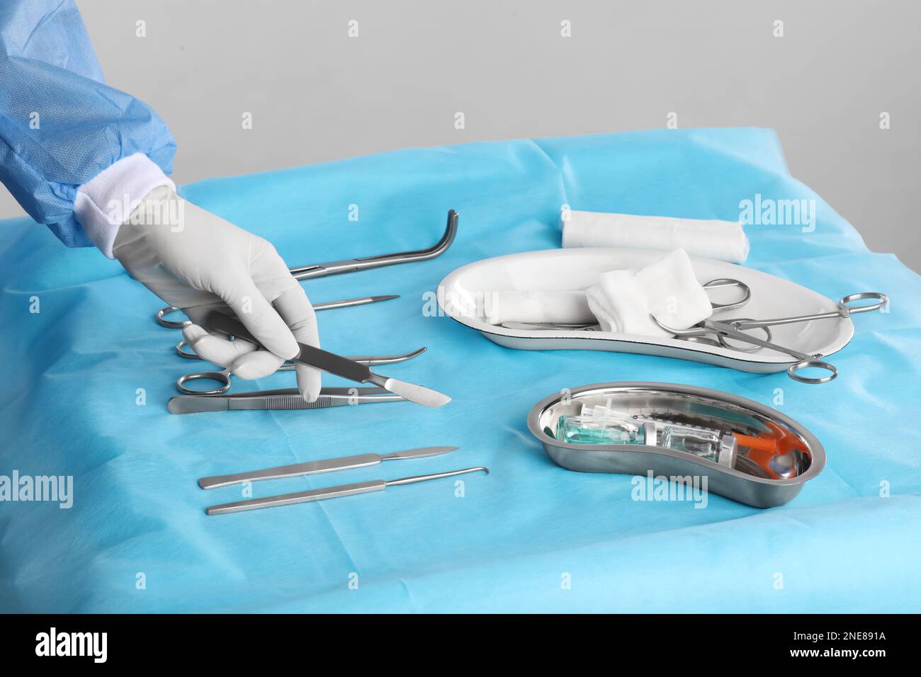 Doctor holding scalpel over table with surgical instruments against light background, closeup Stock Photo