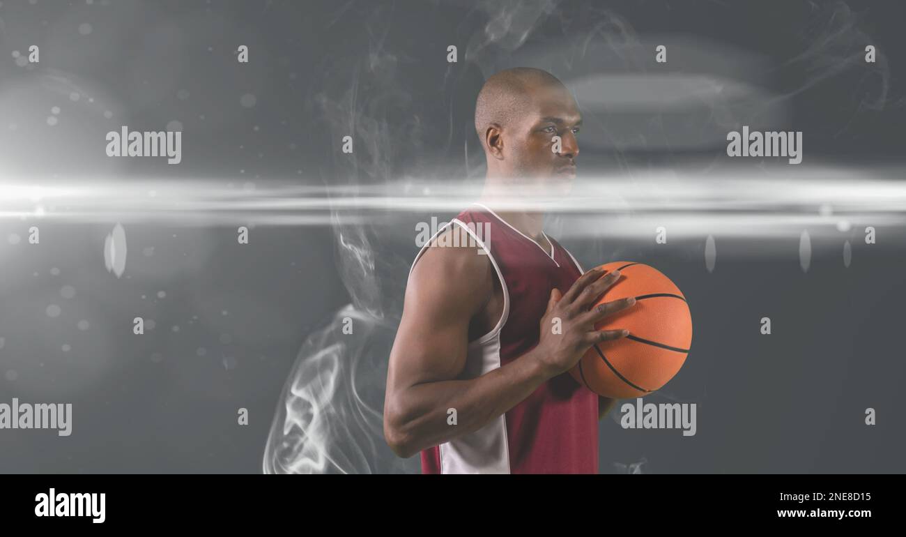 African american male basketball player holding ball against smoke effect on grey background Stock Photo