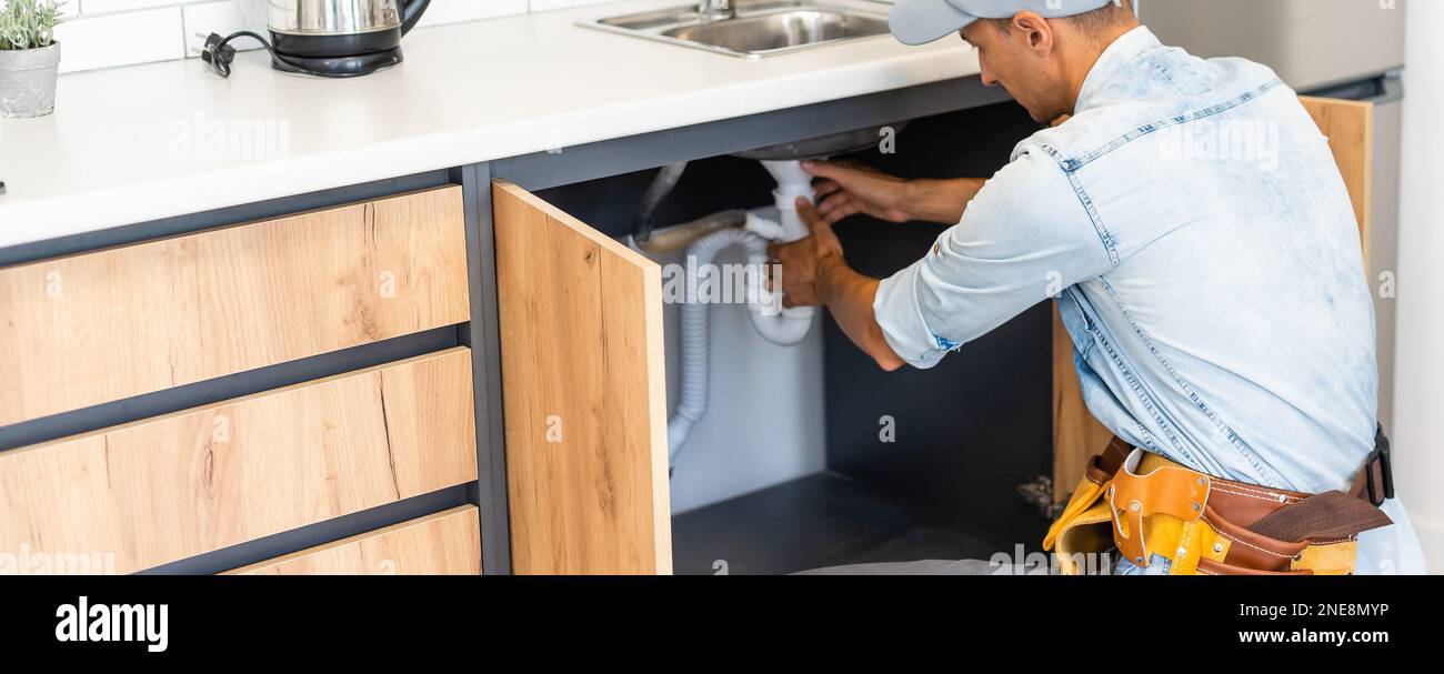 plumber fixes sink siphon by two pipe-wrenches in kitchen. Stock Photo