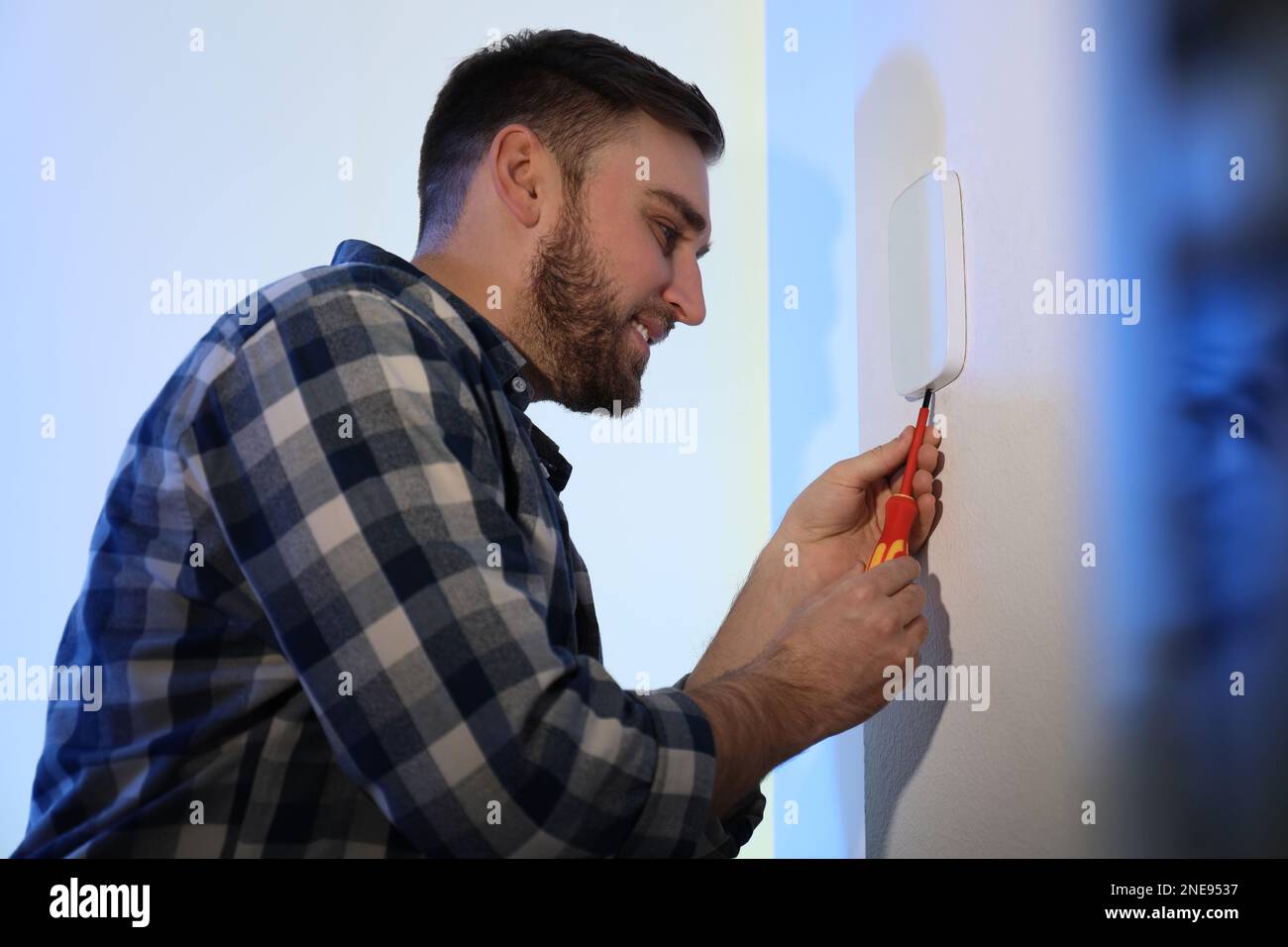 Man installing security alarm system on light wall at home Stock Photo