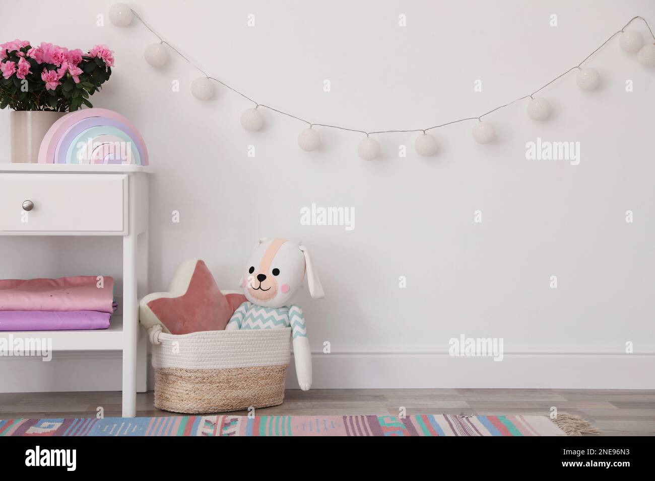 Stand with houseplant and toys near light wall in baby room. Interior ...