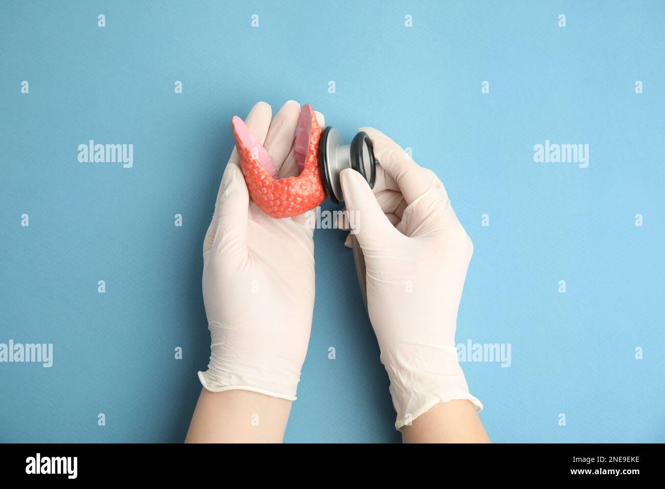 Doctor with stethoscope examining healthy thyroid on light blue background, top view Stock Photo