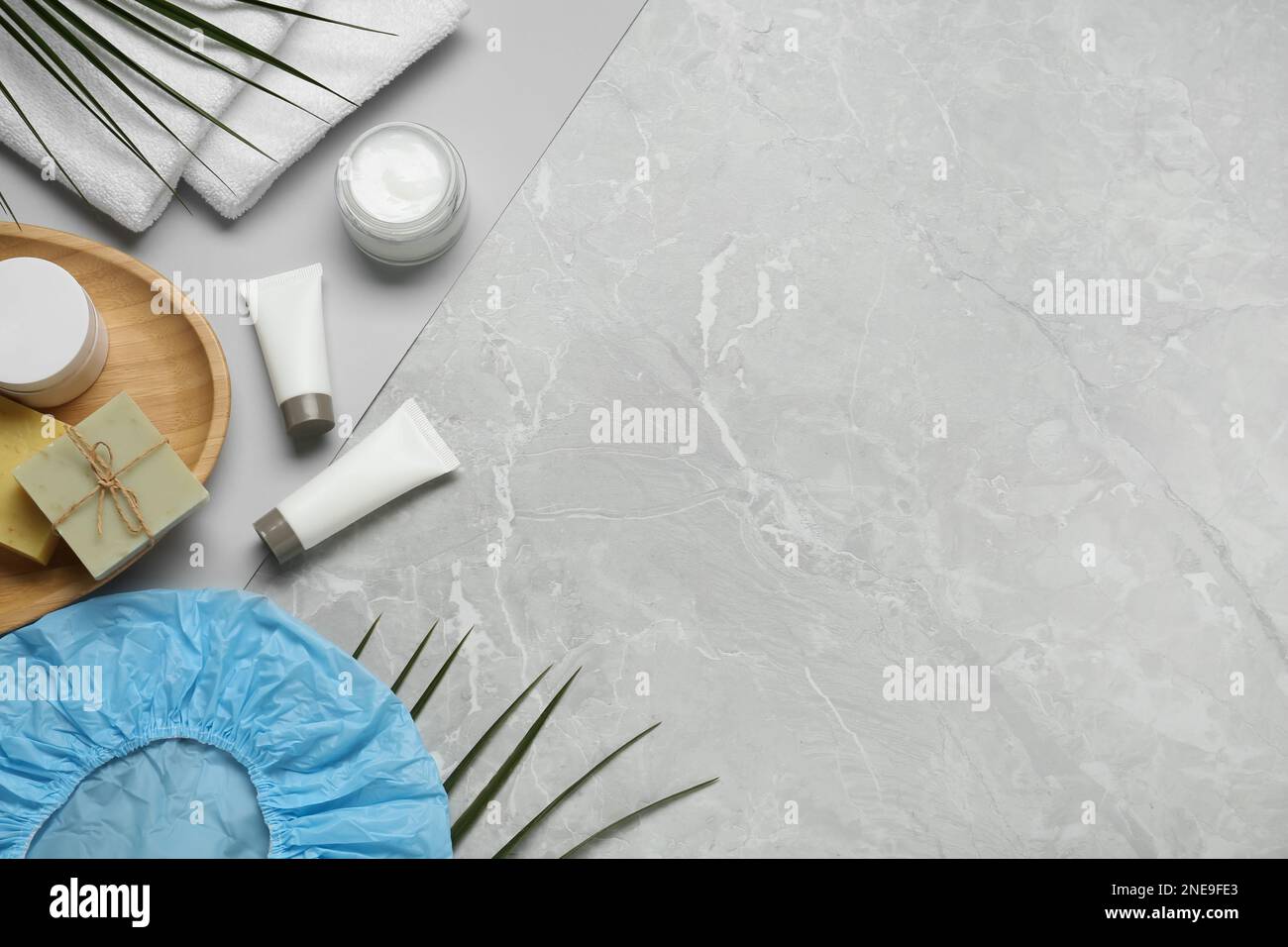 Flat lay composition with shower cap and toiletries on grey marble ...