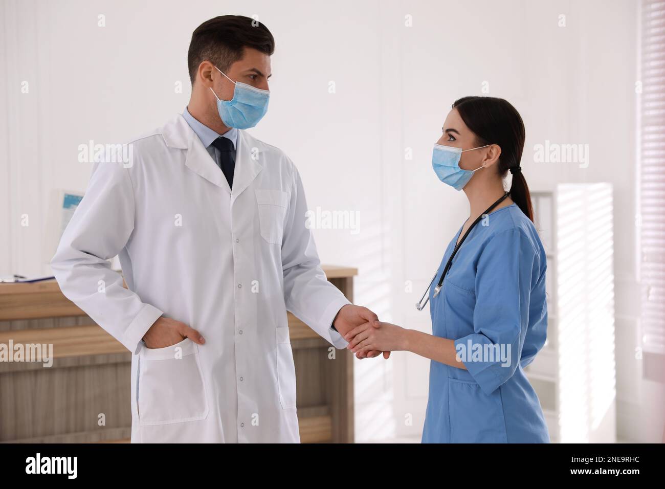 Doctors with protective masks giving handshake in clinic Stock Photo
