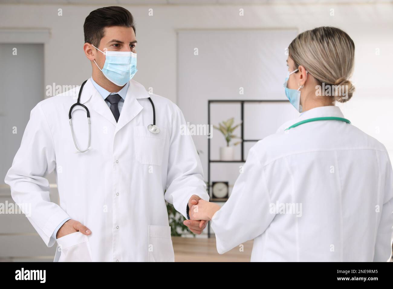 Doctors with protective masks giving handshake in clinic Stock Photo