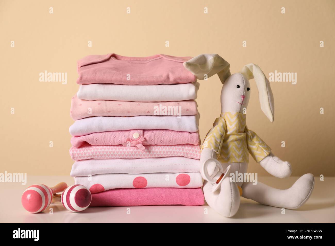 Stack of baby girl's clothes, rattles, pacifier and toy bunny on white ...