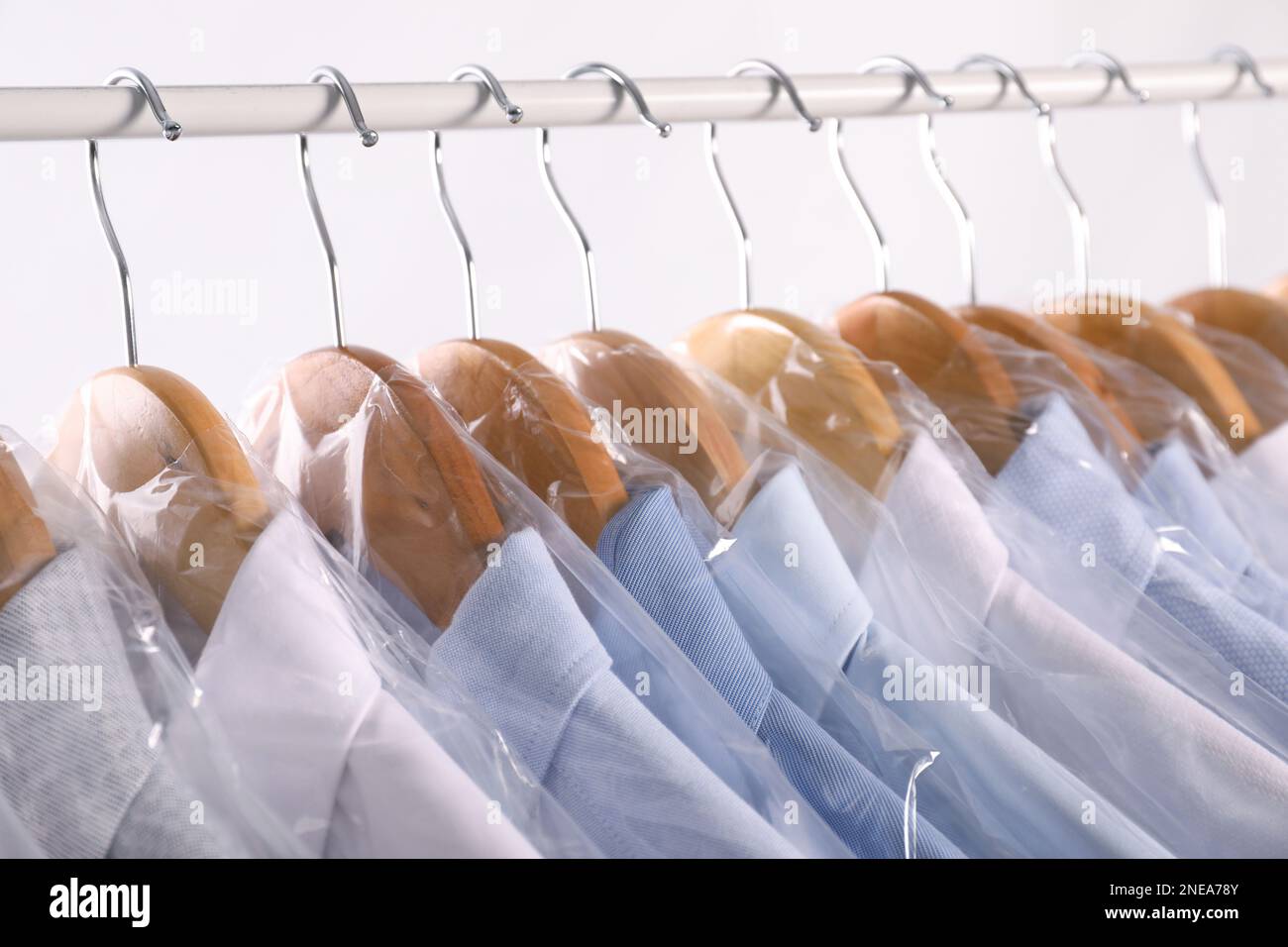 https://c8.alamy.com/comp/2NEA78Y/hangers-with-shirts-in-dry-cleaning-plastic-bags-on-rack-against-light-background-closeup-2NEA78Y.jpg