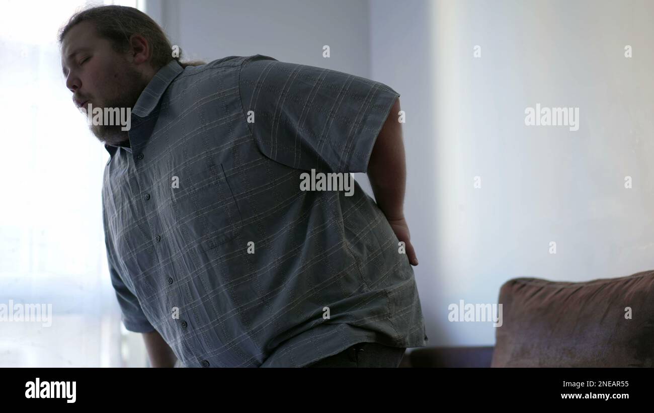 Man having back pain. One overweight person getting up from couch and