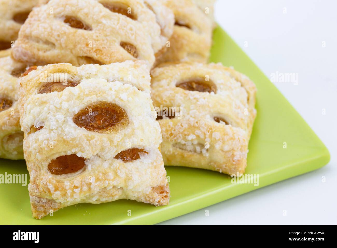 Close up of fresh, baked apple strudel, tempting sweet bites, on light green square plate against white background Stock Photo