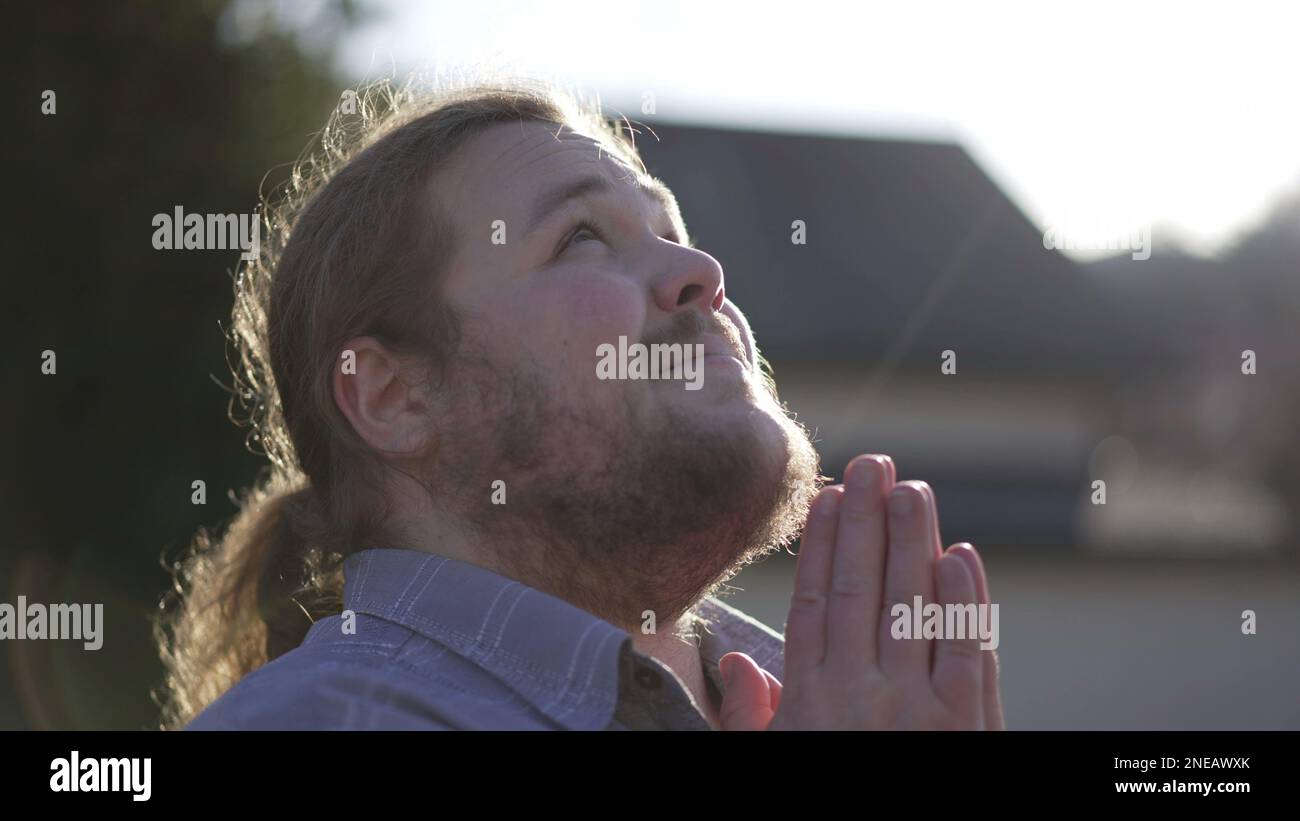 One religious overweight young man in prayer outdoors closing eyes in