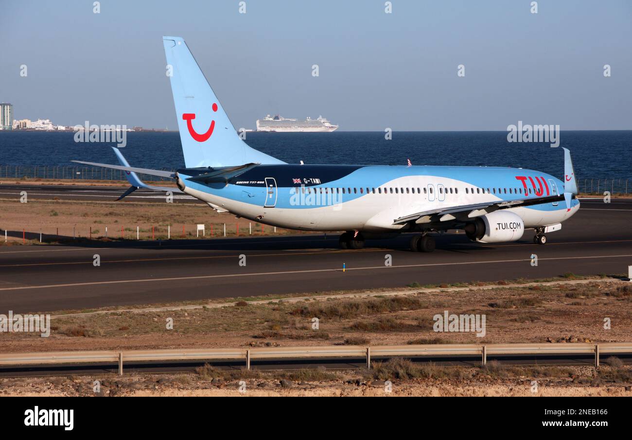 A Boeing 737-800 of TUI lines up to depart Lanzarote Arrecife Airport Canary Islands with a cruise ship to the rear Stock Photo