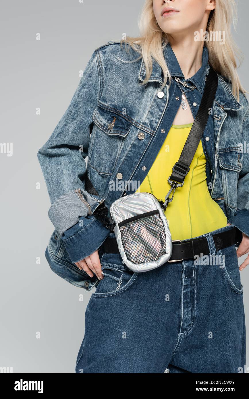 cropped view of blonde woman in stylish denim jacket with belt bag posing isolated on grey,stock image Stock Photo