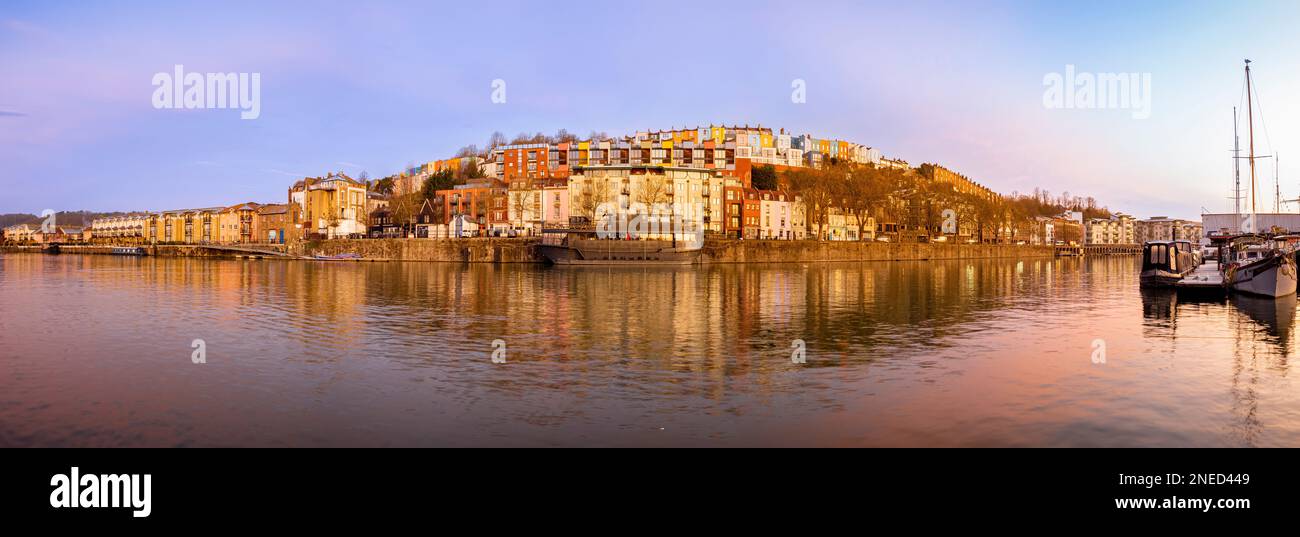 Panoramic view of the Grain Barge floating bar and restaurant with rows of colourful houses behind, seen from the marina looking North at sunrise. UK Stock Photo