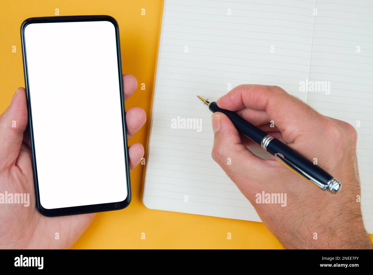 top view of person taking notes on paper while using smartphone, template with copy space Stock Photo
