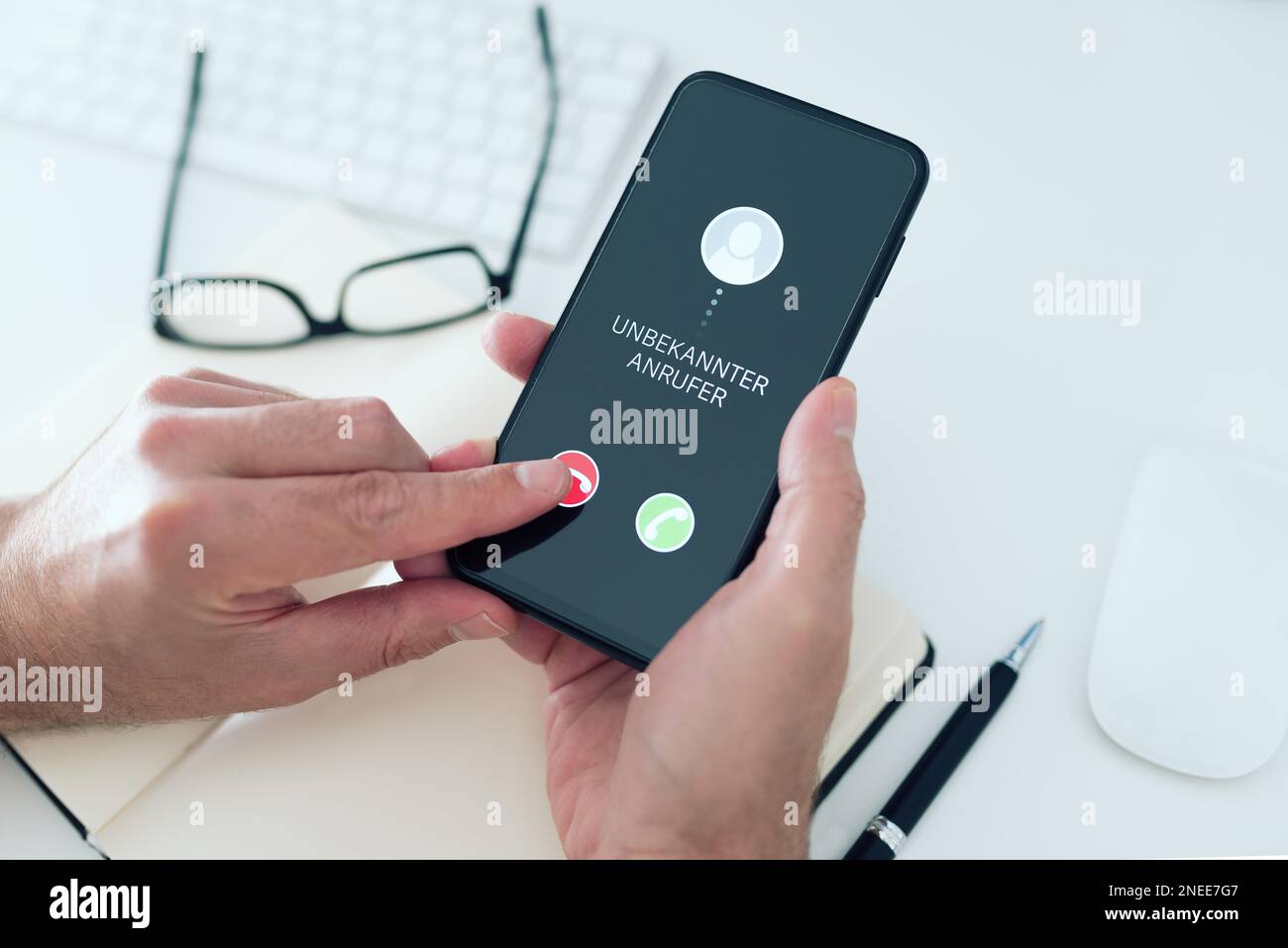 close-up view of person rejecting call from unknown number with text UNBEKANNTER ANRUFER, German for unknown caller, on smartphone, phone scam and Stock Photo
