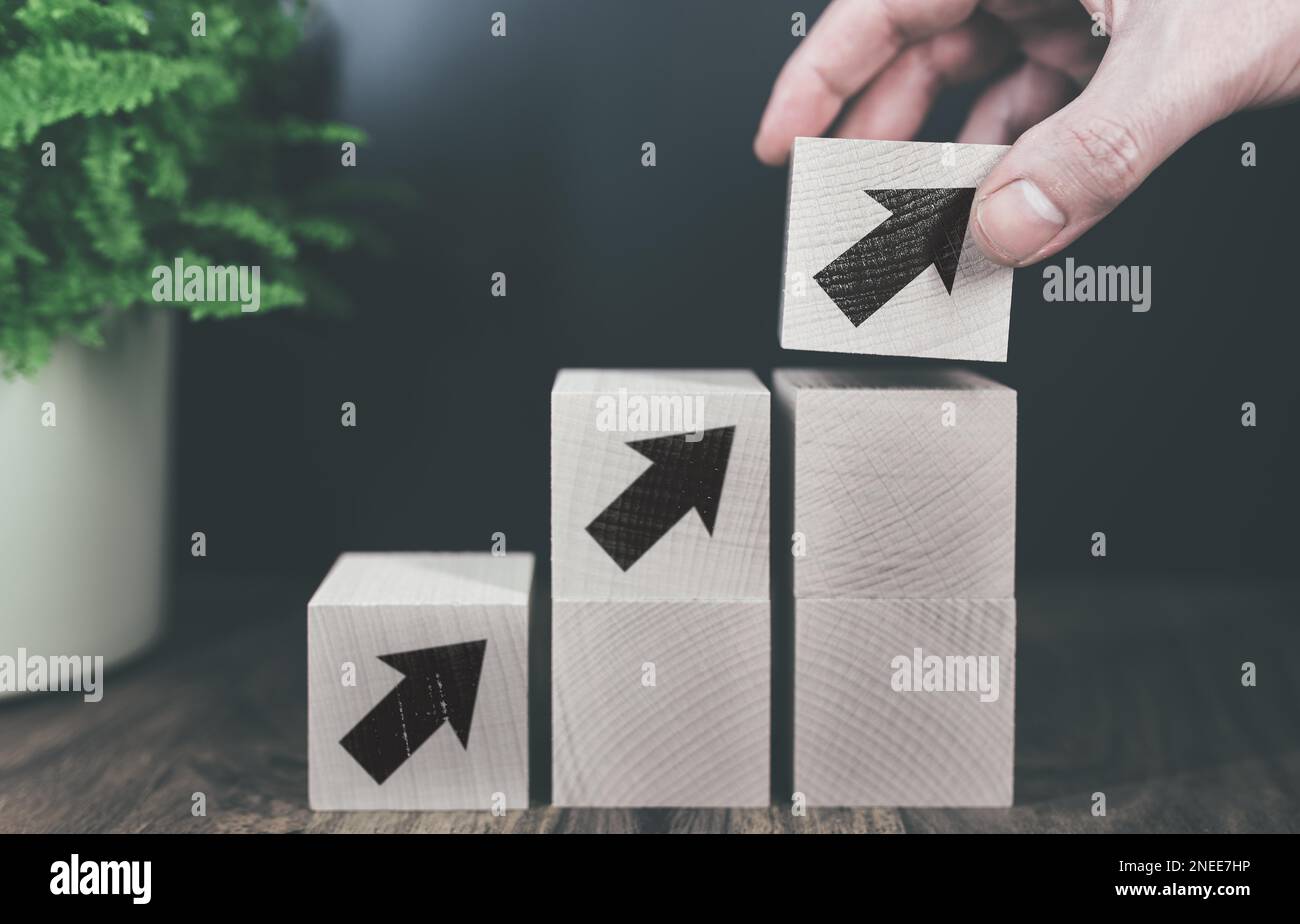 close-up of hand stacking wooden blocks with arrow symbol in steps, business or economic growth concept Stock Photo
