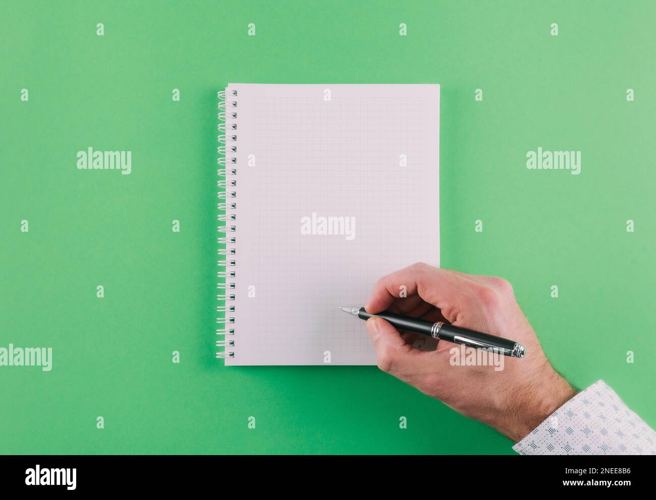 top view of hand holding ballpoint pen against spiral notepad on green background, taking notes concept Stock Photo