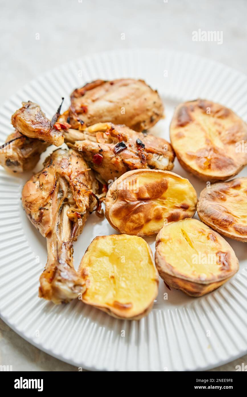 Chicken baked in pieces with potatoes and onion on a white dish. Home