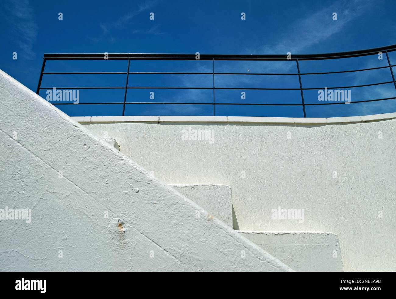 White wall, stairs, and black railings,against a blue sky with light