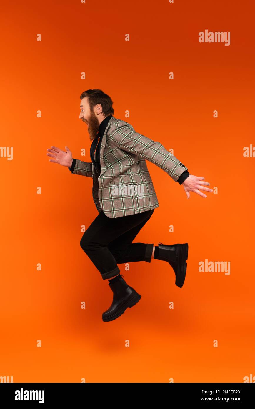 Side view of excited stylish man jumping on red background,stock image Stock Photo